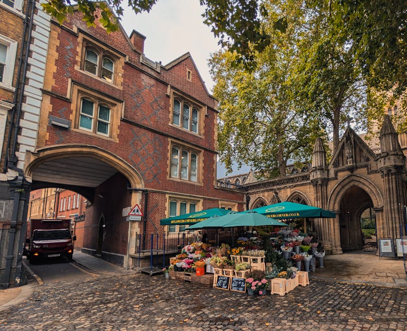 A flower stall situated on a cobblestone street in North Kensington, featuring an array of fresh floral arrangements and bouquets displayed under a green canopy with the text 'flower delivery northken