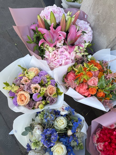A selection of beautifully arranged floral bouquets, each wrapped in elegant white or pink paper, featuring a variety of fresh flowers. The prominent bouquet at the top showcases large pink lilies wit