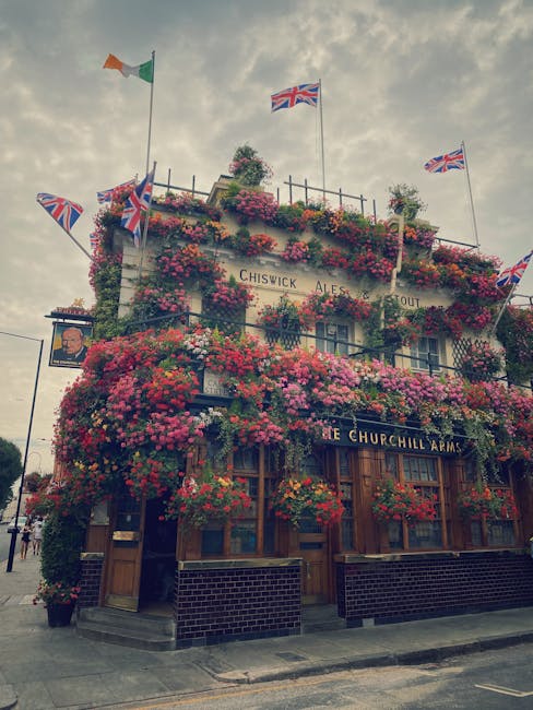 An exterior view of the Churchill Arms pub, adorned with an abundant display of colorful flowers including pink and purple petunias and red geraniums cascading around the windows and balcony. Several