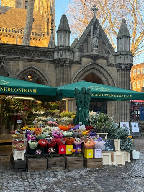 A vibrant flower stall set up outdoors in front of an historic stone building with gothic architectural features in North Kensington. The display includes fresh flowers arranged in colorful bouquets w